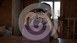 Boy think at the table near the tablet, clutching his head, insoluble situation