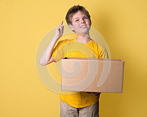 Boy thinking holding a box on yellow background. Think out of th