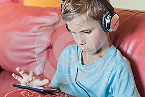 the boy is thinking and listening to music,playing,doing homework online with smartphone.Pupil in headphones