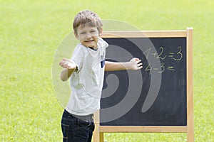 Boy thinking, writing and counting on blackboard. Green outdoor background