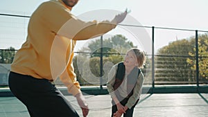 Boy throwing ball playing with father on the basketball court on a sunny day