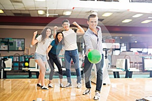 Boy Throwing Bowling Ball While Friends Cheering In Club