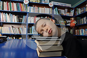 Boy tired sleeping on pile of books in library exausted on education