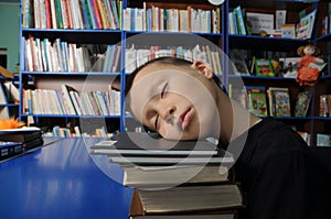 Boy tired sleeping on pile of books in library exausted of education