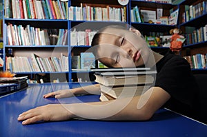 Boy tired sleeping on pile of books in library exausted to learning photo