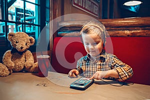 Boy toddler playing with digital gadget phone with earphones