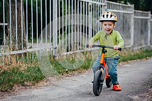 The boy todler rides a runner and laughs. The boy wears a helmet.