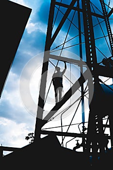 Boy on top of a metal tower posing with the sky in the background. Black silhouette of a man on a tall metal structure doing