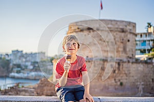 Boy tourist eating turkish ice cream on background of Hidirlik Tower in Antalya against the backdrop of the photo