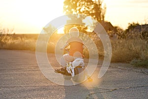 Boy on toy bike rides on the road. Summer, sunset. Back view