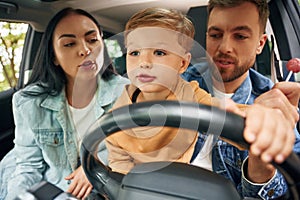 Boy is trying to ride. Family of father, mother and little son are sitting in the modern car