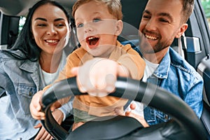 Boy is trying to ride. Family of father, mother and little son are sitting in the modern car