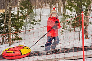 Boy with tubing rises on a travelator to the mountain. Child having fun on snow tube. Boy is riding a tubing. Winter fun