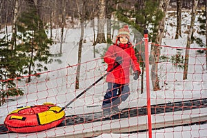 Boy with tubing rises on a travelator to the mountain. Child having fun on snow tube. Boy is riding a tubing. Winter fun