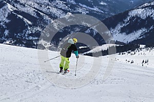 Boy is turning on other side for next arc on skies. A male skier skiing freeride in Slovakia mountains, Low Tatras. Yellow helmet