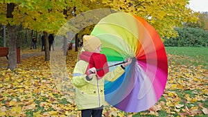 Boy twists bright multi-colored umbrella in autumn park. Happy autumn time. Family is walking in the park. Beautiful