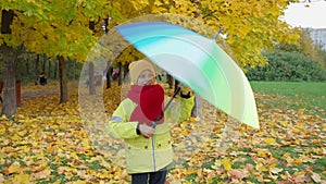 Boy twists bright multi-colored umbrella in autumn park. Happy autumn time. Family is walking in the park. Beautiful