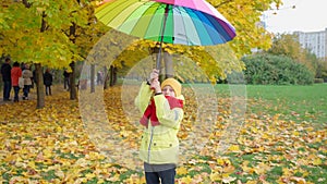 Boy twists bright multi-colored umbrella in autumn park. Happy autumn time. Family is walking in the park. Beautiful