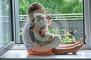 Boy of two years sitting by the window and hugs a toy Bunny. rainy weather, waiting for dad to come home from work