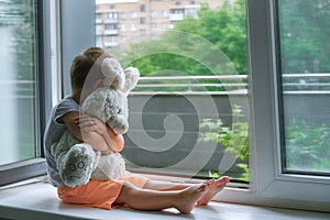 Boy of two years sitting by the window and hugs a toy Bunny. rainy weather, waiting for dad to come home from work