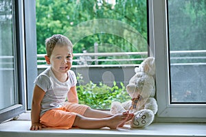 Boy of two years sitting by the window and hugs a toy Bunny. rainy weather, waiting for dad to come home from work