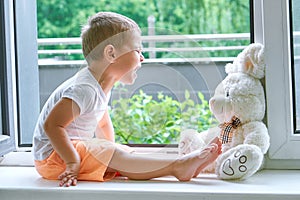 Boy of two years sitting by the window and hugs a toy Bunny. rainy weather, waiting for dad to come home from work