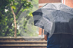 A boy under a black umbrella in the heavy rainy day with face in backwards