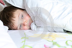 Boy under the blanket. Sad child boy looks out from under the covers