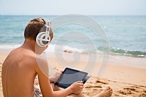 Boy uses a Tablet PC sitting on a beach