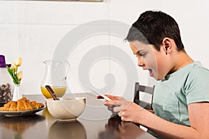 Boy using digital tablet during breakfast in kitchen