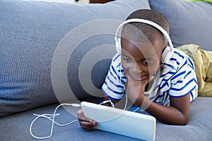 Boy using digital tablet while listening to headphones on sofa at home