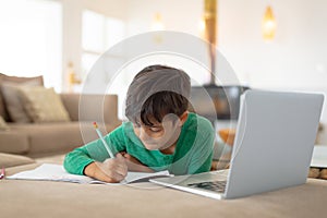 Boy using laptop while drawing a sketch on book at home