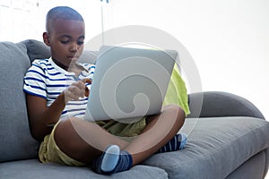 Boy using laptop while sitting with crossed legged on sofa at home