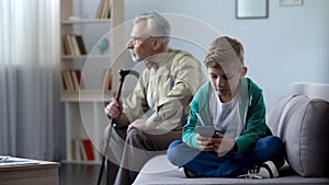 Boy using mobile phone, upset granddad sitting aside, internet addiction concept