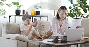 Boy using phone and interrupting mother working from home