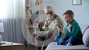 Boy using smartphone, upset granddad sitting aside, internet addiction concept