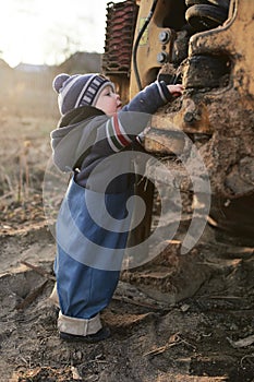 A boy in the village on the background of a tractor walks on the sand .