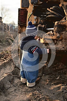 A boy in the village on the background of a tractor walks on the sand .