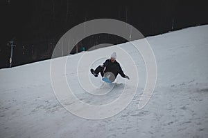 Boy from the village in a white cap rode down the slope on a plastic snowboard to a jumper and jumps. Man in a jump. Enjoying