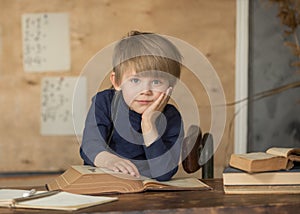 Boy in vintage clothes sits at a table with books