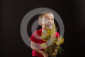 a boy with vitiligo in a red T-shirt with a bouquet of mimosa
