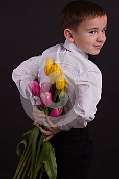 The boy with vitiligo in white shirt and a bow tie with tulips on a black Studio background