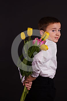 The boy with vitiligo in white shirt and a bow tie with tulips on a black Studio background