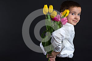 The boy with vitiligo in white shirt and a bow tie with tulips on a black Studio background