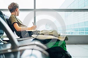 Boy waits departure time in airport and writes in notebook