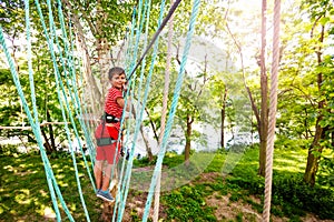 Boy walk on ropes between trees in adventure park