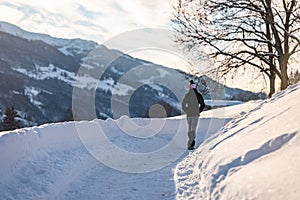 Boy walking alone on empty snow-covered road in winter towards the mountains.