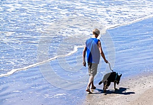 Teenage boy walks his dog on a beach near the edge of the ocean