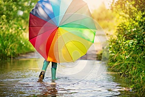 Boy walking through the puddle with colorful umbrella in his hands.