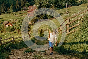 A boy walks along a dirt road in a village in the summer in the Alpine mountains.